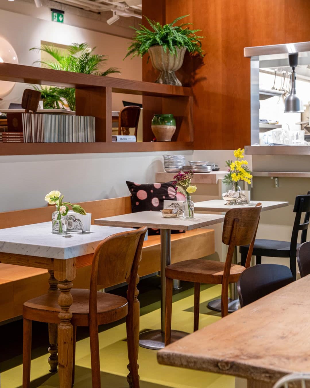 Eine Sitzecke mit Holzbank, Bistrotischen und kleinen Blumensträussen