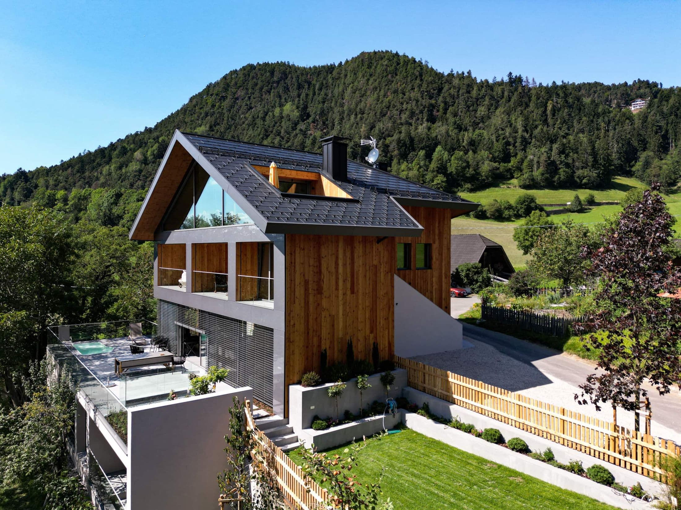 Die Baules Alpine Lodge von oben: Holzhaus mit Glasgiebel, Terrasse mit Pool und Garten am Waldrand